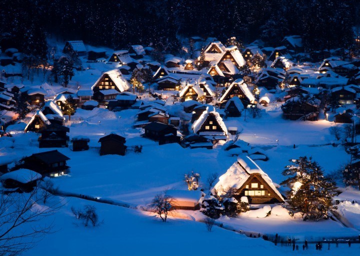 Small village of wooden farmhouses covered in snow at night