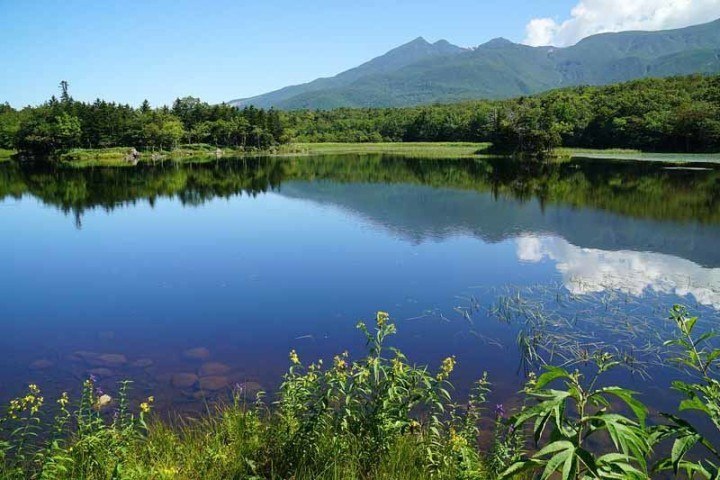 Beautiful lake surrounded by mountains and forest reflecting blue sky